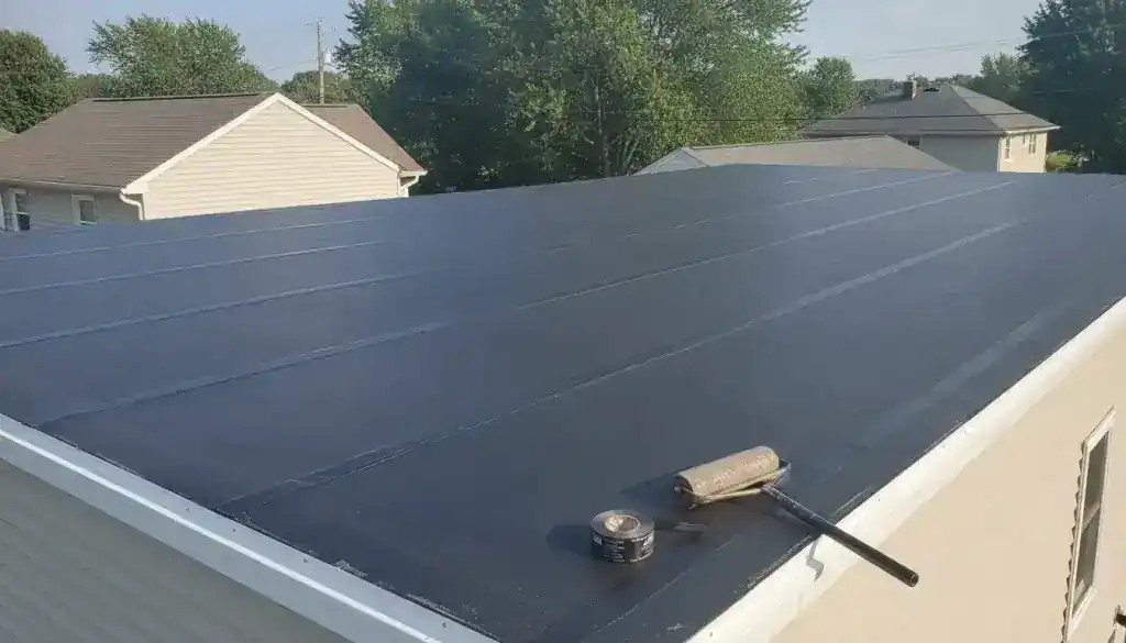 A flat roof covered with a dark membrane, a seam roller and a roll of tape resting on the surface. Illustrative image.